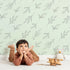 Lovely child standing in front of Whimsy Tots Leaf Outline Symphony Wallpaper in Mint Green with leaf, branch, botanical, outline in design.