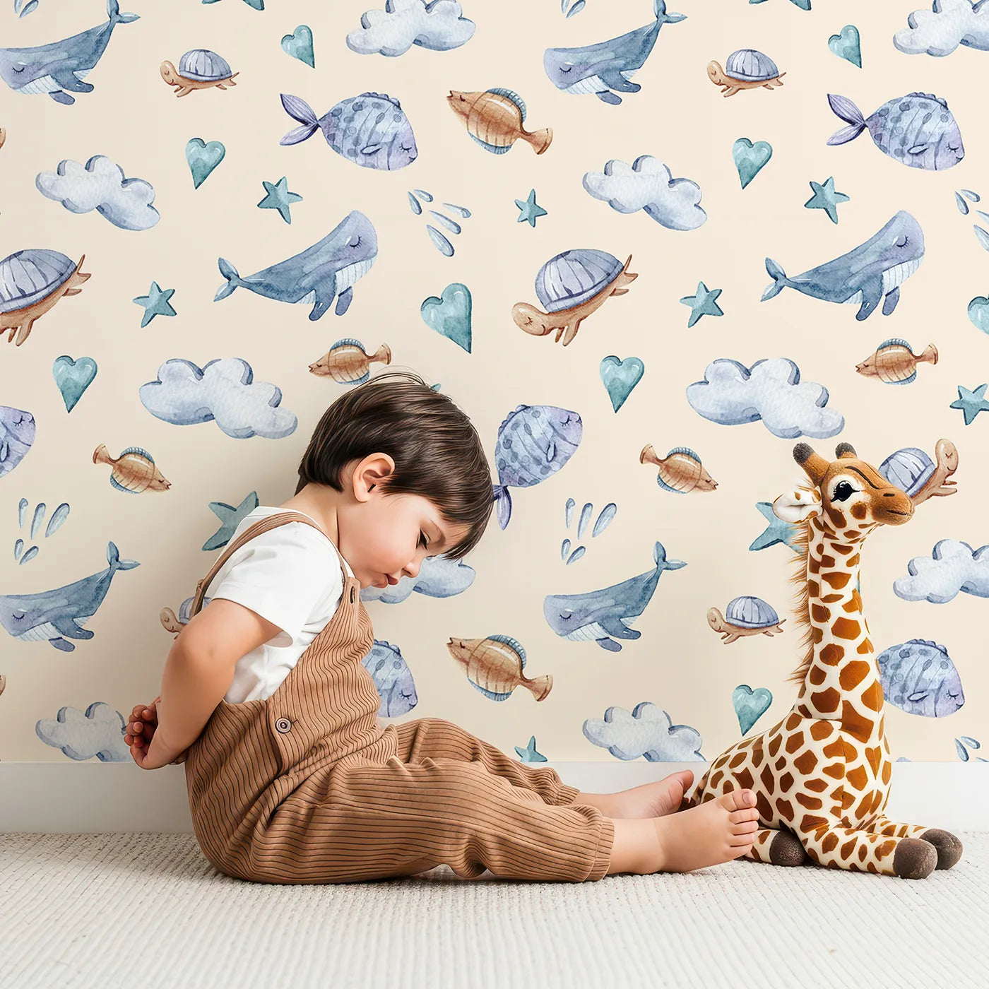 Lovely child standing in front of Whimsy Tots Sleepy Sea Sky Wallpaper in Sand with whale, turtle, fish, cloud, star, heart in design.