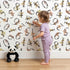 Lovely child standing in front of Whimsy Tots Botanical Numbers Wallpaper in White with number, leaf, foliage, vine in design.