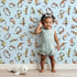 Lovely child standing in front of Whimsy Tots Botanical Numbers Wallpaper in Blue with number, leaf, vine, foliage in design.