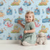 Lovely child standing in front of Whimsy Tots Undersea Island Adventure Wallpaper in Blue with whale, turtle, dolphin, octopus, fish, starfish, shrimp, submarine, bottle, island in design.