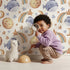 Lovely child standing in front of Whimsy Tots Sleepy Celestial Whale Wallpaper in White with whale, moon, star, fish, comet in design.