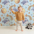 Lovely child standing in front of Whimsy Tots Sleepy Celestial Whale Wallpaper in Blue with whale, moon, star, fish, comet in design.