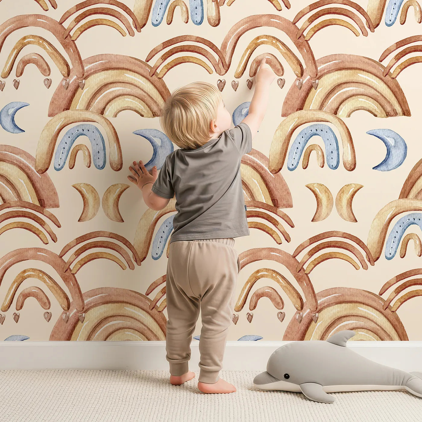 Lovely child standing in front of Whimsy Tots Boho Rainbow Night Wallpaper in Sand with rainbow, moon, heart, arch in design.