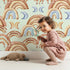 Lovely child standing in front of Whimsy Tots Boho Rainbow Night Wallpaper in Mint Green with rainbow, moon, heart, arch in design.
