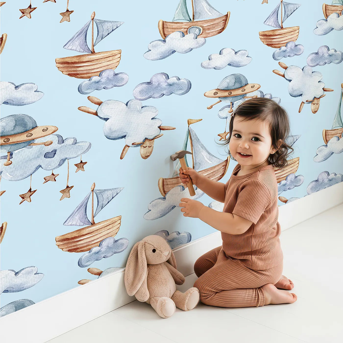 Lovely child standing in front of Whimsy Tots Counting Clouds and Sailing Dreams Wallpaper in Blue with sheep, boat, cloud, star, mobile in design.