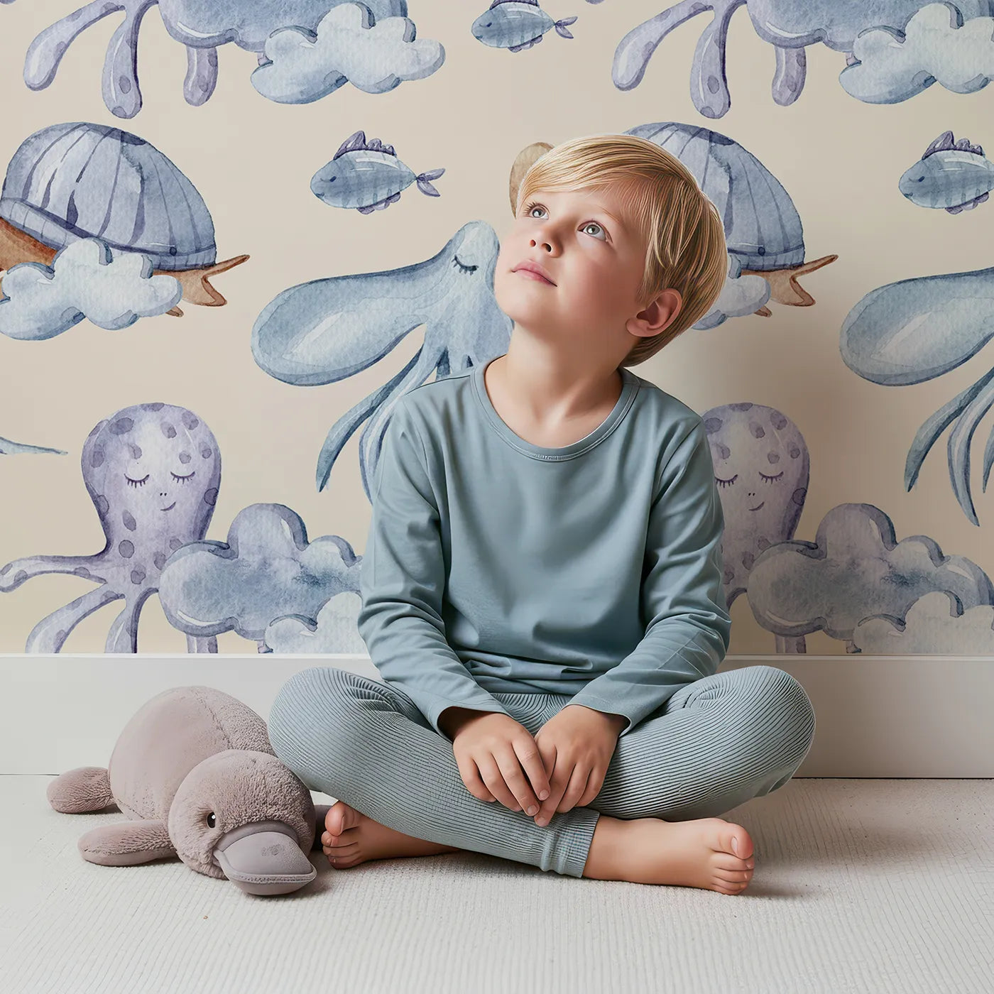 Lovely child standing in front of Whimsy Tots Ocean Cloud Cuddle Wallpaper in Beige with turtle, octopus, fish, cloud, squid in design.