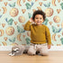 Lovely child standing in front of Whimsy Tots Lunar Lullaby Birds Wallpaper in Mint Green with bird, moon, heart in design.