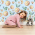 Lovely child standing in front of Whimsy Tots Lunar Lullaby Birds Wallpaper in Sky Blue with bird, moon, heart in design.
