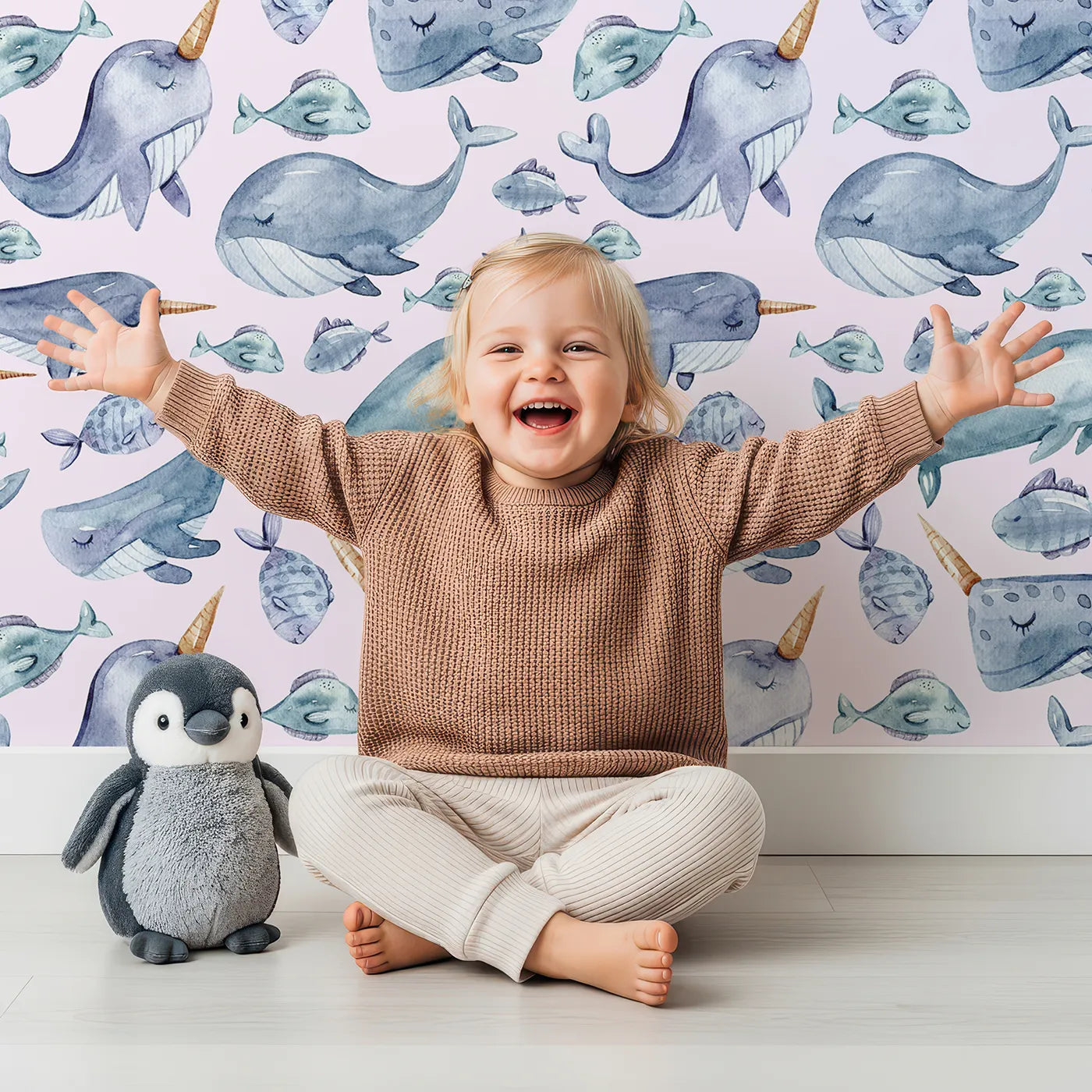 Lovely child standing in front of Whimsy Tots Sleepy Sea Friends Wallpaper in Blush Pink with whale, narwhal, fish in design.