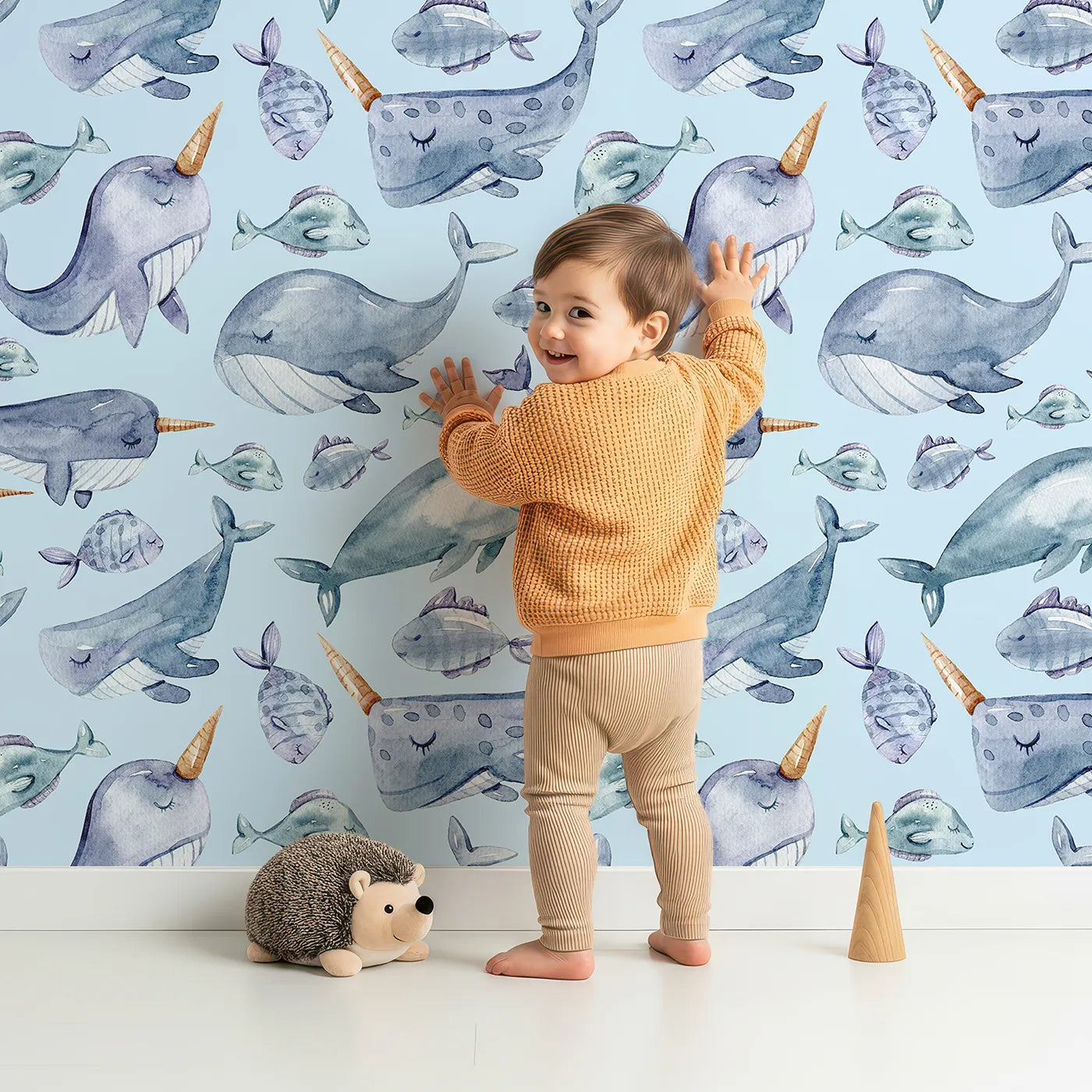 Lovely child standing in front of Whimsy Tots Sleepy Sea Friends Wallpaper in Sky Blue with whale, narwhal, fish in design.