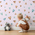 Lovely child standing in front of Whimsy Tots Heartful Whimsy Wallpaper in Blush Pink with heartful, whimsy, wallpaper in design.