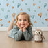 Lovely child standing in front of Whimsy Tots Heartful Whimsy Wallpaper in Sky with heart in design.