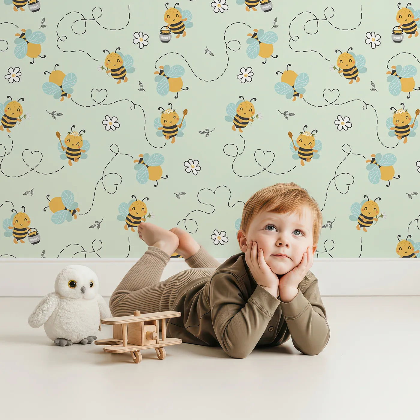 Lovely child standing in front of Whimsy Tots Busy Bees at Play Wallpaper in Mint Green with bee, flower, heart, honey in design.