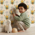 Lovely child standing in front of Whimsy Tots Bee Blossom Parade Wallpaper in Sand with bee, flower, honey in design.