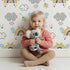 Lovely child standing in front of Whimsy Tots Bee Rainbow Dreams Wallpaper in White with bee, rainbow, star, cloud in design.