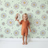 Lovely child standing in front of Whimsy Tots Daisy Dot Dance Wallpaper in Mint Green with flower, dot in design.