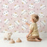 Lovely child standing in front of Whimsy Tots Royal Kitty Wink Wallpaper in Pink with cat, heart, crown in design.