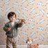 Lovely child standing in front of Whimsy Tots Royal Kitty Wink Wallpaper in Peach with cat, heart, crown in design.