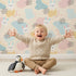 Lovely child standing in front of Whimsy Tots Bunny Bounce Abstract Wallpaper in Buttercream with bunny, blob, heart, texture in design.