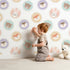 Lovely child standing in front of Whimsy Tots Woodland Buddy Portraits Wallpaper in White with bear, fox, owl, bunny, flower, wreath in design.
