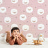 Lovely child standing in front of Whimsy Tots Sleepy Stardust Sheep Wallpaper in Rose Pink with sheep, star, cloud, swirl in design.