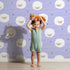 Lovely child standing in front of Whimsy Tots Sleepy Stardust Sheep Wallpaper in Lavender Mist with sheep, star, cloud, swirl in design.