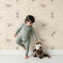 Lovely child standing in front of Whimsy Tots Safari Nap Bubbles Wallpaper in Peach Beige with elephant, zebra, lion, giraffe, hippo, bubble, circle in design.