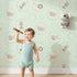 Lovely child standing in front of Whimsy Tots Safari Nap Bubbles Wallpaper in Mint Green with elephant, zebra, lion, giraffe, hippo, bubble, circle in design.