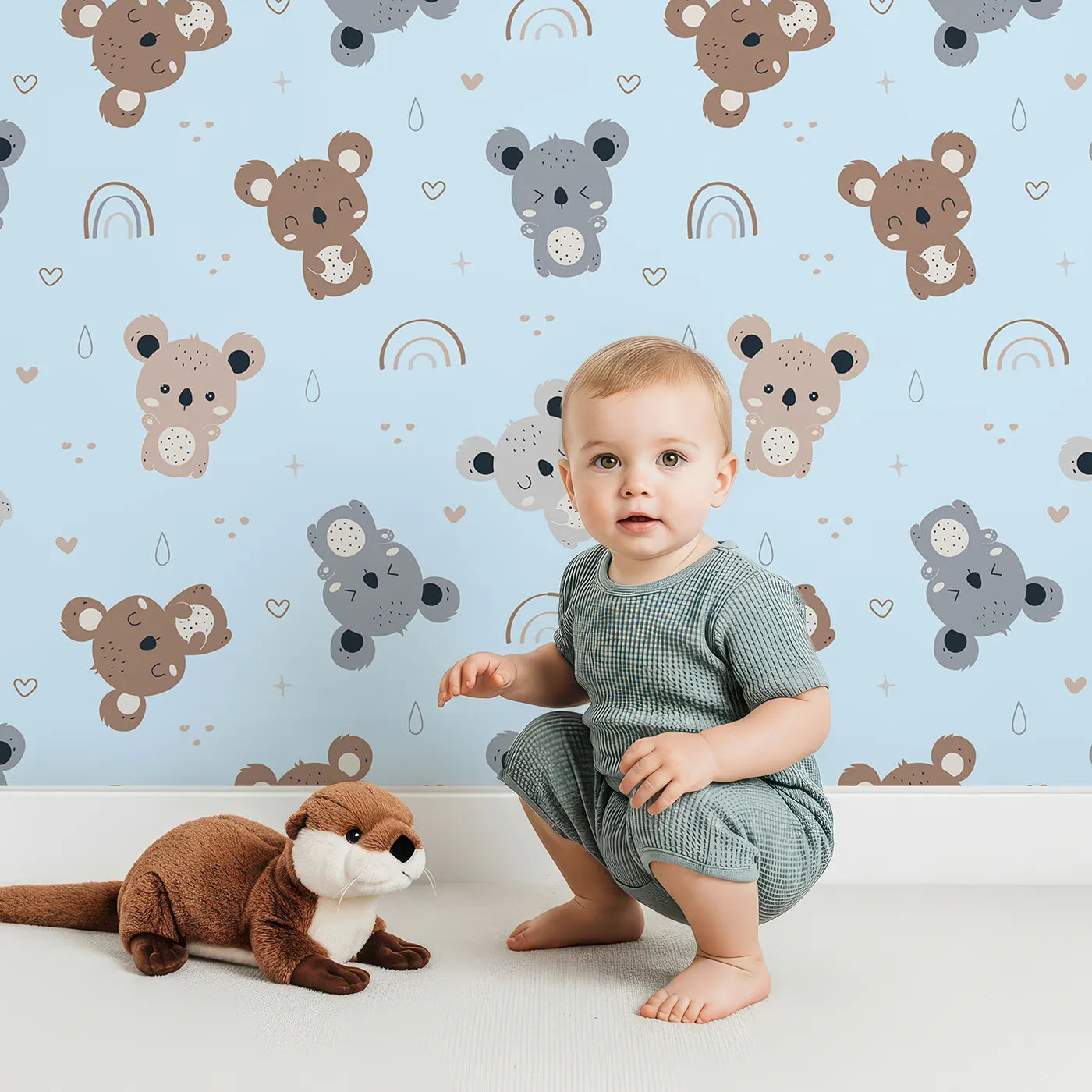 Lovely child standing in front of Whimsy Tots Koala Cuddle Parade Wallpaper in Blue with koala, rainbow, heart, raindrop in design.