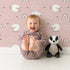 Lovely child standing in front of Whimsy Tots Sleepy Meadow Parade Wallpaper in Rose Blush Pink with sheep, rainbow, cloud, star in design.