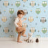 Lovely child standing in front of Whimsy Tots Gentle Owl Garden Wallpaper in Sky Blue with owl, flower, leaf in design.