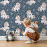 Lovely child standing in front of Whimsy Tots Feathered Daydream Unicorn Wallpaper in Navy Blue with unicorn, feather, moon, star, leaf in design.