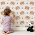Lovely child standing in front of Whimsy Tots Tiger Grid Giggles Wallpaper in Blush Pink with tiger, paw, grid in design.