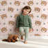 Lovely child standing in front of Whimsy Tots Tiger Grid Giggles Wallpaper in Pink with tiger, paw, grid in design.