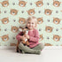 Lovely child standing in front of Whimsy Tots Tiger Grid Giggles Wallpaper in Mint Green with tiger, paw, grid in design.