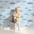 Lovely child standing in front of Whimsy Tots Tiny Toot Toot Cars Wallpaper in Blue with car, vehicle, pastel, transportation in design.