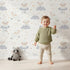 Lovely child standing in front of Whimsy Tots Counting Sheep Dreams Wallpaper in White with sheep, star, cloud, night sky in design.