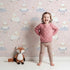 Lovely child standing in front of Whimsy Tots Counting Sheep Dreams Wallpaper in Blush Pink with sheep, star, cloud, night sky in design.