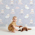 Lovely child standing in front of Whimsy Tots Counting Sheep Dreams Wallpaper in Lavender with sheep, star, cloud, night sky in design.
