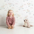 Lovely child standing in front of Whimsy Tots Little Lamb Hops Wallpaper in Soft Sky with sheep, star, cloud, sky in design.