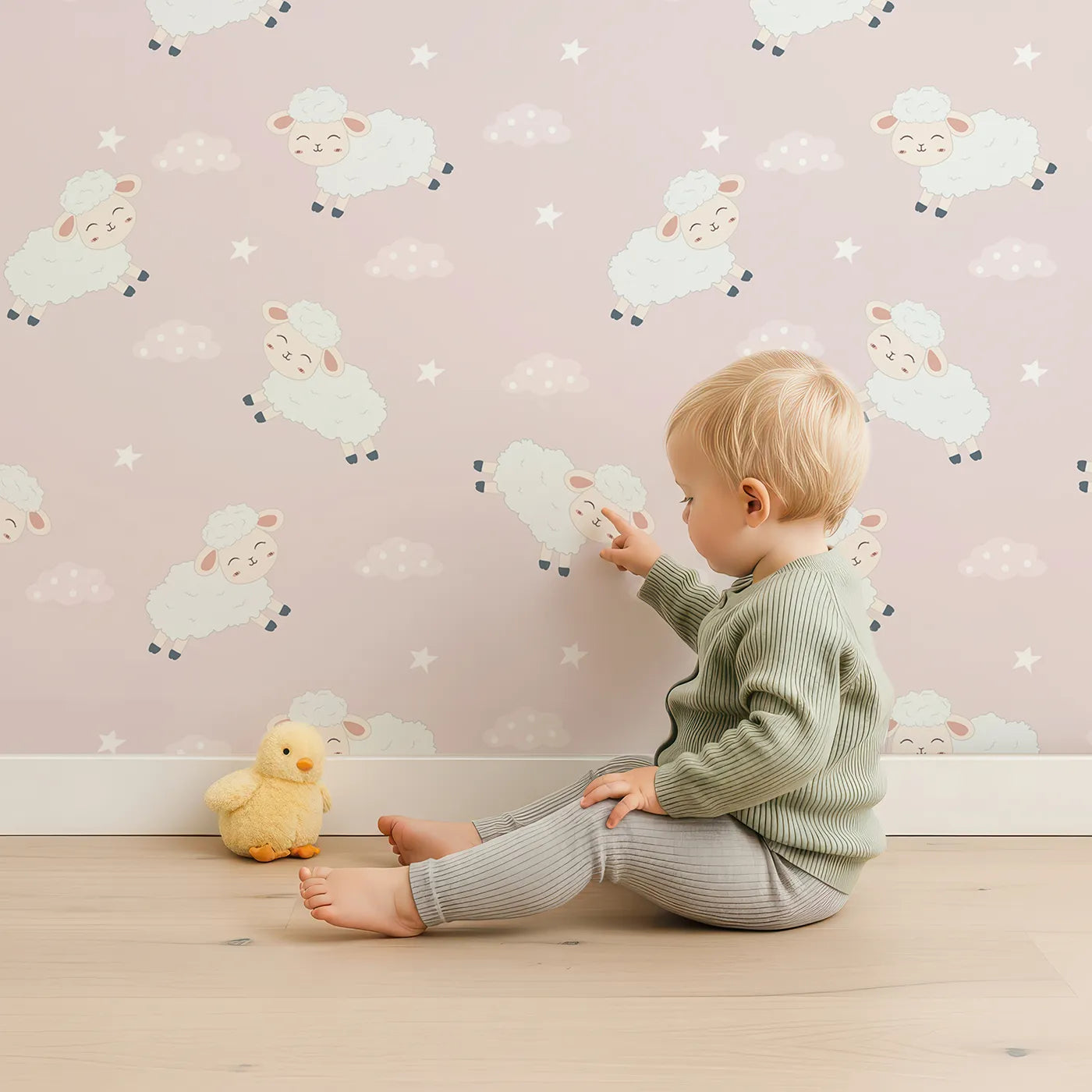 Lovely child standing in front of Whimsy Tots Little Lamb Hops Wallpaper in Blush Pink with sheep, star, cloud, sky in design.