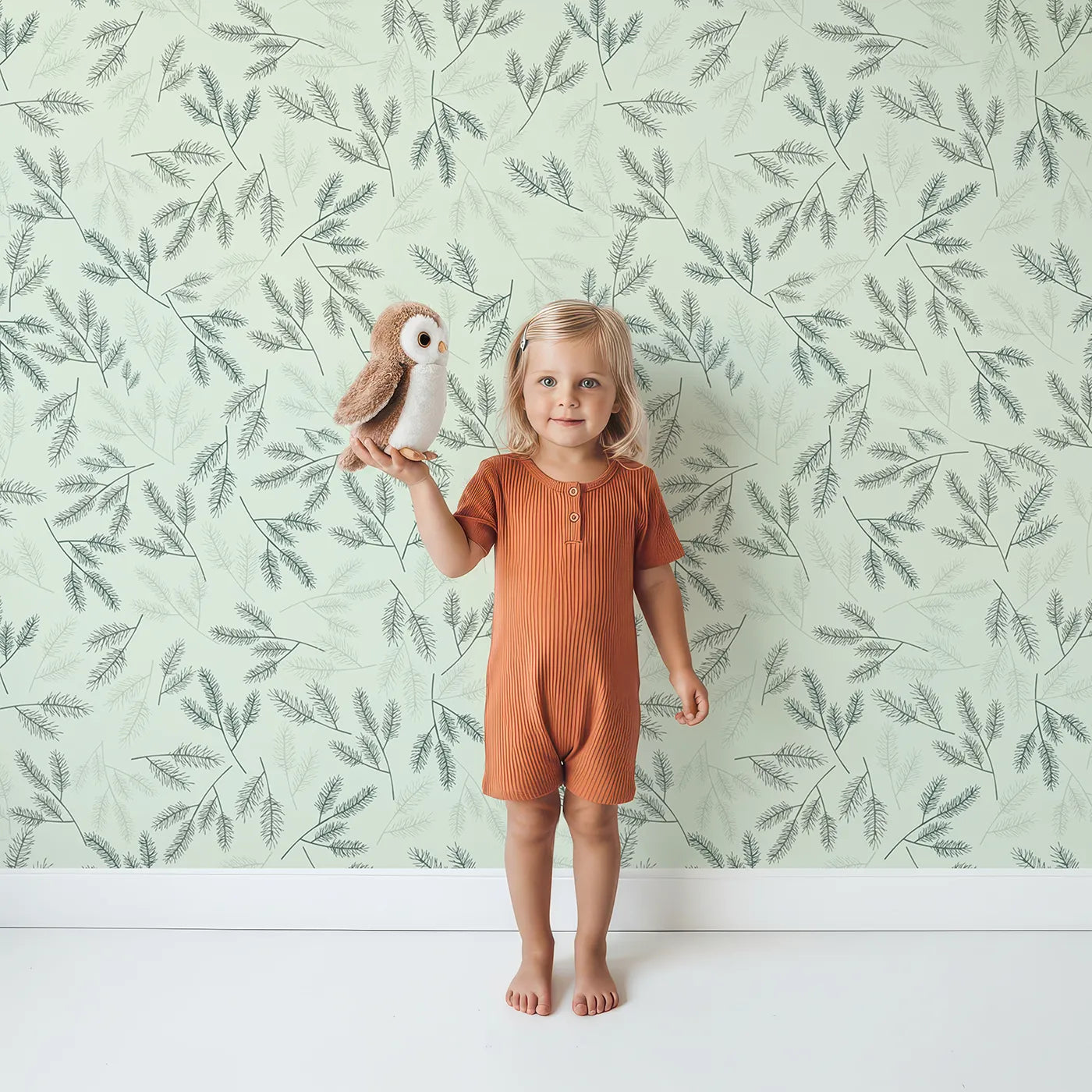 Lovely child standing in front of Whimsy Tots Whispering Ferns Wallpaper in Sage Green with fern, leaf, branch, foliage in design.