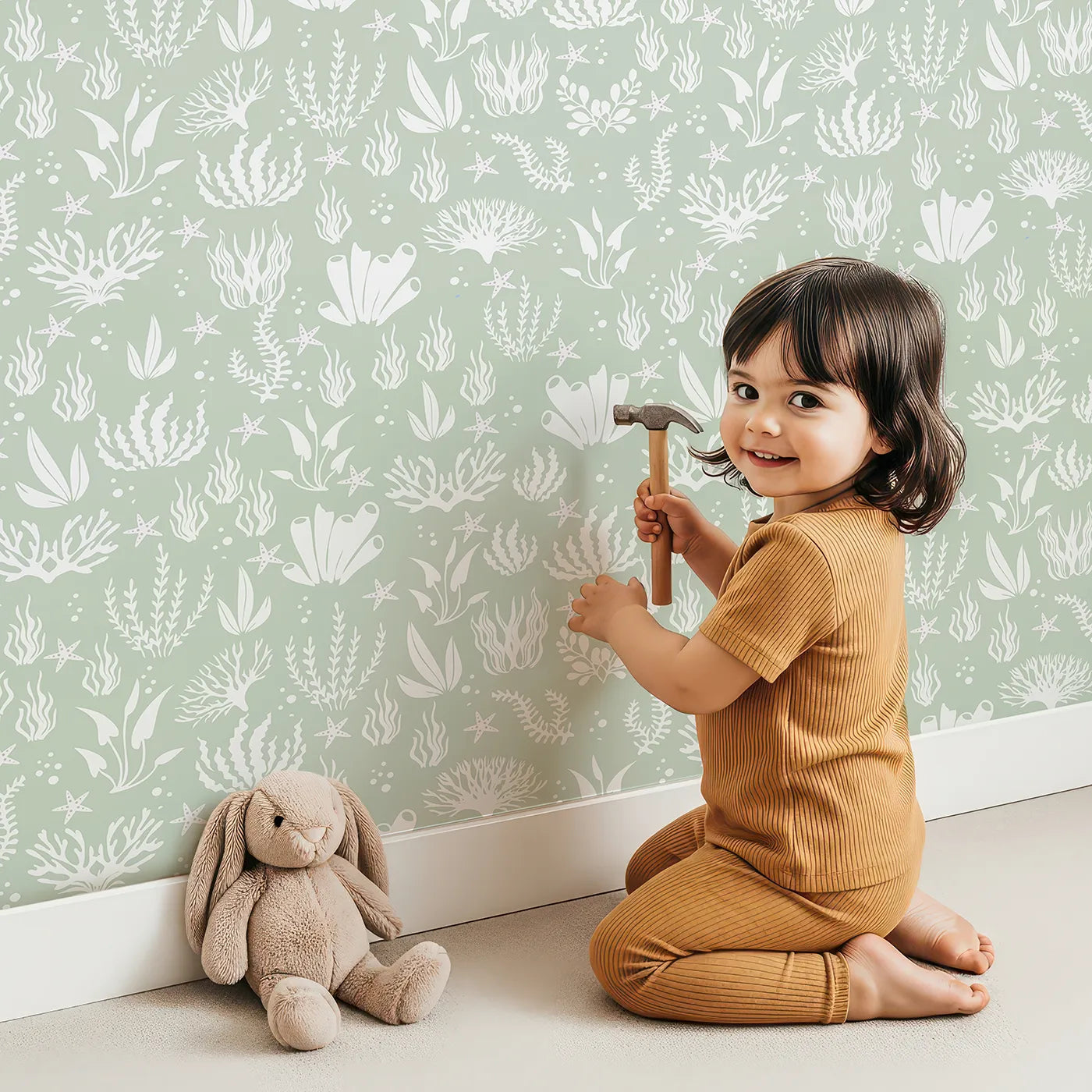Lovely child standing in front of Whimsy Tots Coral Garden Dance Wallpaper in Seafoam Green with coral, seaweed, starfish, bubble in design.