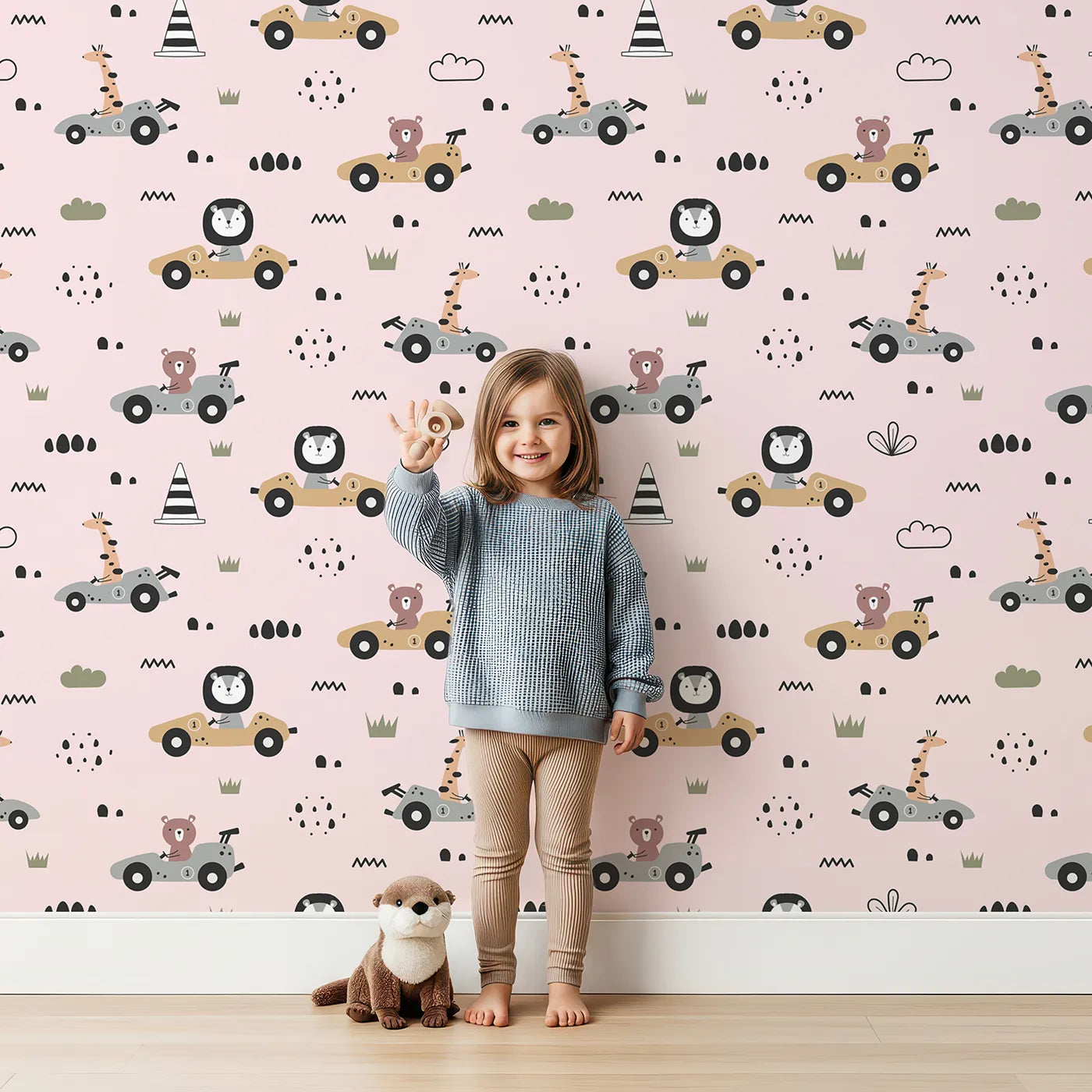 Lovely child standing in front of Whimsy Tots Safari Racers Parade Wallpaper in Blush Pink with lion, giraffe, bear, car, road, wheel in design.