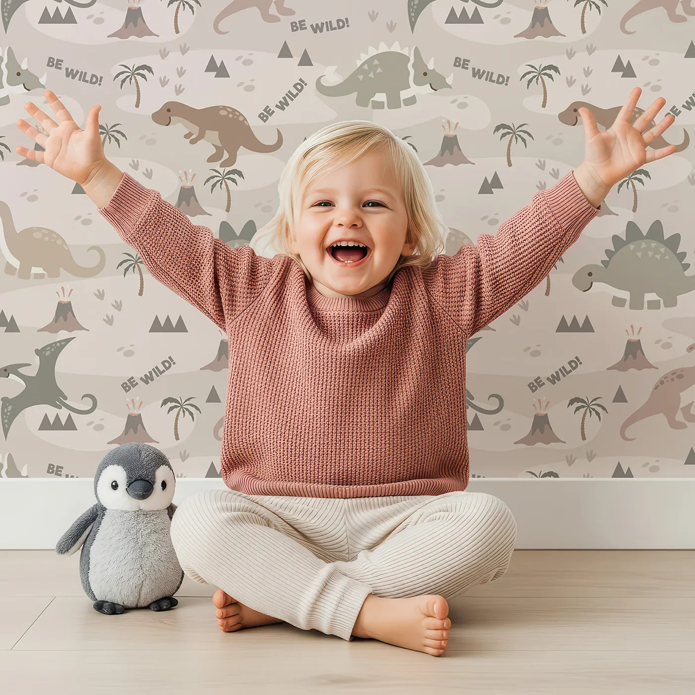 Lovely child standing in front of Whimsy Tots Dino Explorer Land Wallpaper in Sand with dinosaur, volcano, tree, mountain in design.