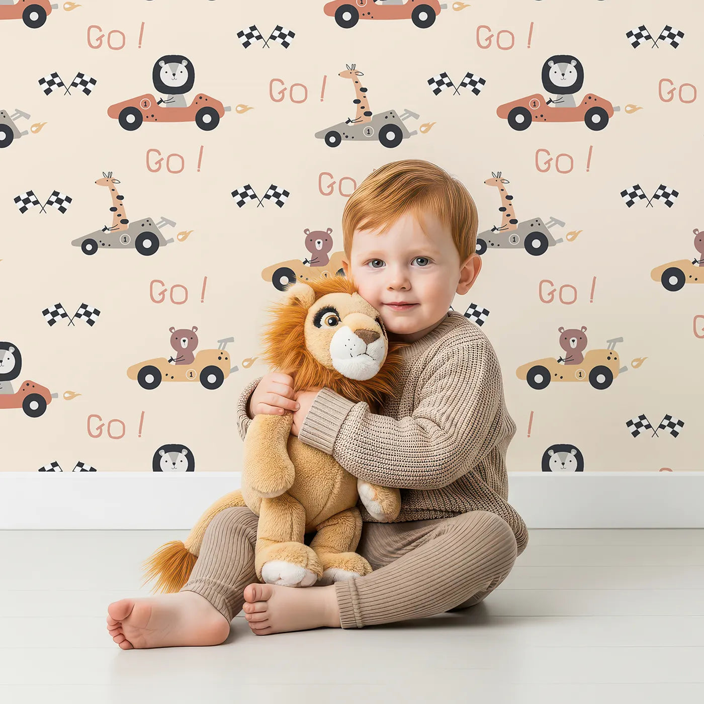 Lovely child standing in front of Whimsy Tots Animal Racers Wallpaper in Warm Beige with giraffe, bear, lion, car, racecar, flag in design.