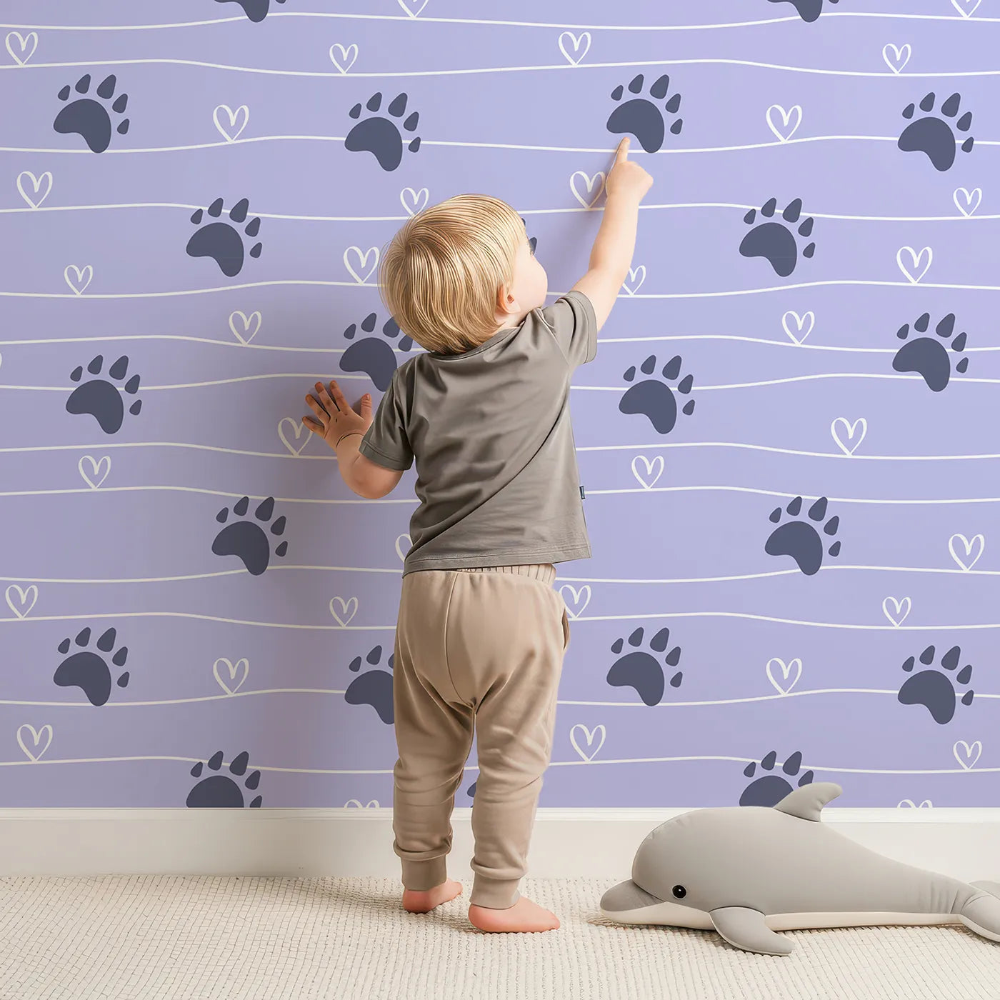 Lovely child standing in front of Whimsy Tots Bear Hug Trail Wallpaper in Lavender Mist with bear, paw print, heart, trail in design.