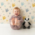 Lovely child standing in front of Whimsy Tots Dino Stomp Parade Wallpaper in Soft Sandstone with dinosaur, footprint, dot, triangle, heart in design.