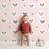 Lovely child standing in front of Whimsy Tots Cuddly Koala Circle Wallpaper in Blush Pink with koala, heart, circle, dot, face in design.